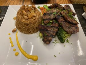 Plate of grilled meat with seasoned rice, broccoli, carrots, and sauce at an Egyptian restaurant