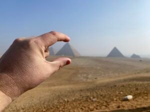 Hand posed in forced perspective as if pinching a distant pyramid on the Giza Plateau with other pyramids beyond