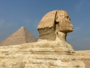 Side profile of the Great Sphinx of Giza with one of the pyramids rising behind it