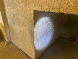 Narrow stone passage covered with hieroglyphs and lit by a flashlight inside an ancient Egyptian tomb