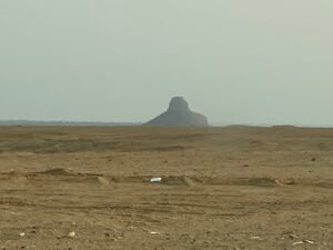 Distant eroded pyramid ruins rising from the flat desert landscape near Dahshur