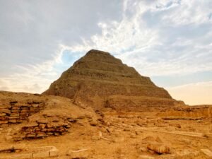 Step Pyramid of Djoser rising behind low stone ruins and sandy archaeological remains at Saqqara
