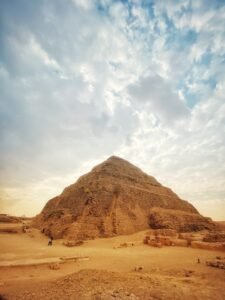 Step Pyramid of Djoser rising above sandy ruins at Saqqara beneath a broad cloud-filled sky