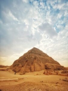 Step Pyramid of Djoser rising above sandy ruins at Saqqara beneath a broad cloud-filled sky