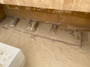 Long stone slab with several repeated carved figures partly surrounded by windblown sand at Saqqara