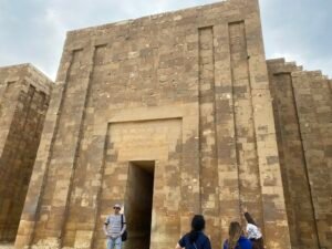 Tall rectangular stone gateway in the Step Pyramid complex at Saqqara with visitors entering below
