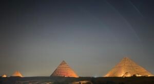 Several pyramids on the Giza Plateau glowing with warm illumination against a dark night sky