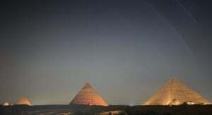 Several pyramids on the Giza Plateau glowing with warm illumination against a dark night sky
