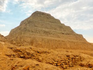 Close view of the weathered stepped masonry of Djoser’s pyramid rising above sandy ruins at Saqqara