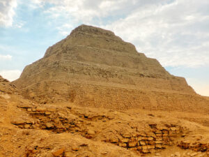 Close view of the weathered stepped masonry of Djoser’s pyramid rising above sandy ruins at Saqqara