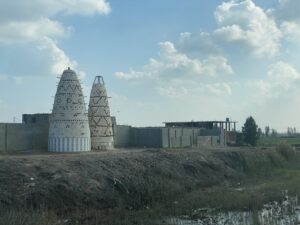Two conical pigeon towers standing beside low buildings and farmland in rural Egypt beneath large clouds