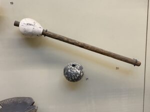 Ancient Egyptian stone mace head mounted on a long wooden haft beside a separate perforated stone mace head in the Egyptian Museum in Cairo
