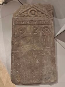 Carved Coptic funerary stela with Greek inscription, central cross, circular motifs and triangular pediment displayed at the Coptic Museum in Cairo