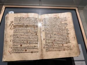Open parchment Christian manuscript written in Coptic script with red rubrics, decorated initials and floral separators, displayed at the Coptic Museum in Old Cairo