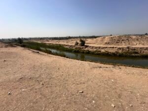Narrow irrigation canal running between sandy desert banks and cultivated vegetation near Lahun, Egypt