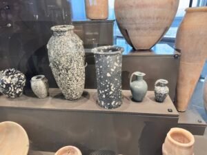 Predynastic Egyptian stone jars and vessels from Neolithic through Naqada II–III grave-good contexts, displayed at the Grand Egyptian Museum in Giza