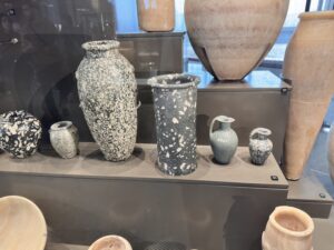 Predynastic Egyptian stone jars and vessels from Neolithic through Naqada II–III grave-good contexts, displayed at the Grand Egyptian Museum in Giza
