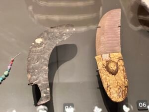 Ancient Egyptian flint knives with curved blades and a decorated handle displayed in a museum case