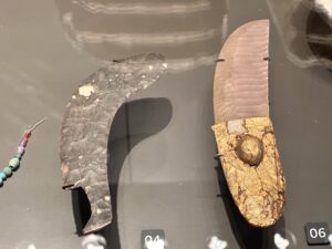 Gebel el-Tarif ceremonial knife, CG 14265, with ripple-flaked flint blade and ivory handle covered in embossed gold leaf, displayed beside another Predynastic flint knife at the Grand Egyptian Museum in Giza