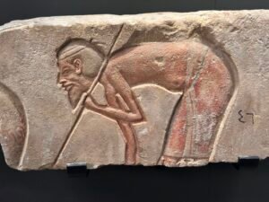 Painted Amarna-period relief fragment showing a bent male figure holding a long staff or pole