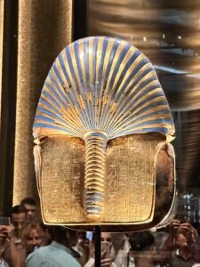 Back of Tutankhamun's golden burial mask, GEM 8, showing the blue-and-gold nemes headdress, braided queue and protective hieroglyphic inscription at the Grand Egyptian Museum in Giza