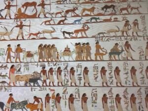 Grand Egyptian Museum display reproducing the Aamu procession from the 12th Dynasty tomb of Khnumhotep II at Beni Hasan, with foreign visitors, animals and hieroglyphic captions