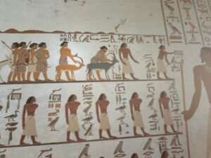 Grand Egyptian Museum reproduction of the Aamu caravan from Khnumhotep II's tomb at Beni Hasan showing foreign visitors in patterned garments leading ibex beneath hieroglyphic captions