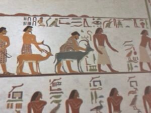 Close detail of the Grand Egyptian Museum reproduction of the Aamu procession from Beni Hasan showing foreign visitors guiding ibex beneath hieroglyphs in Khnumhotep II's tomb scene