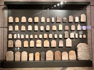 Museum case filled with dozens of small ancient Egyptian stone stelae arranged in rows at the Grand Egyptian Museum