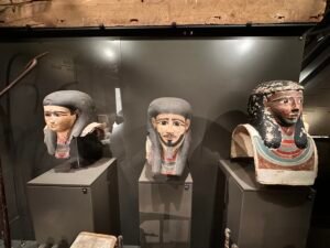 Three Middle Kingdom cartonnage mummy masks displayed together at the Grand Egyptian Museum, including the 11th Dynasty mask of Mesehti, GEM 39209, at center