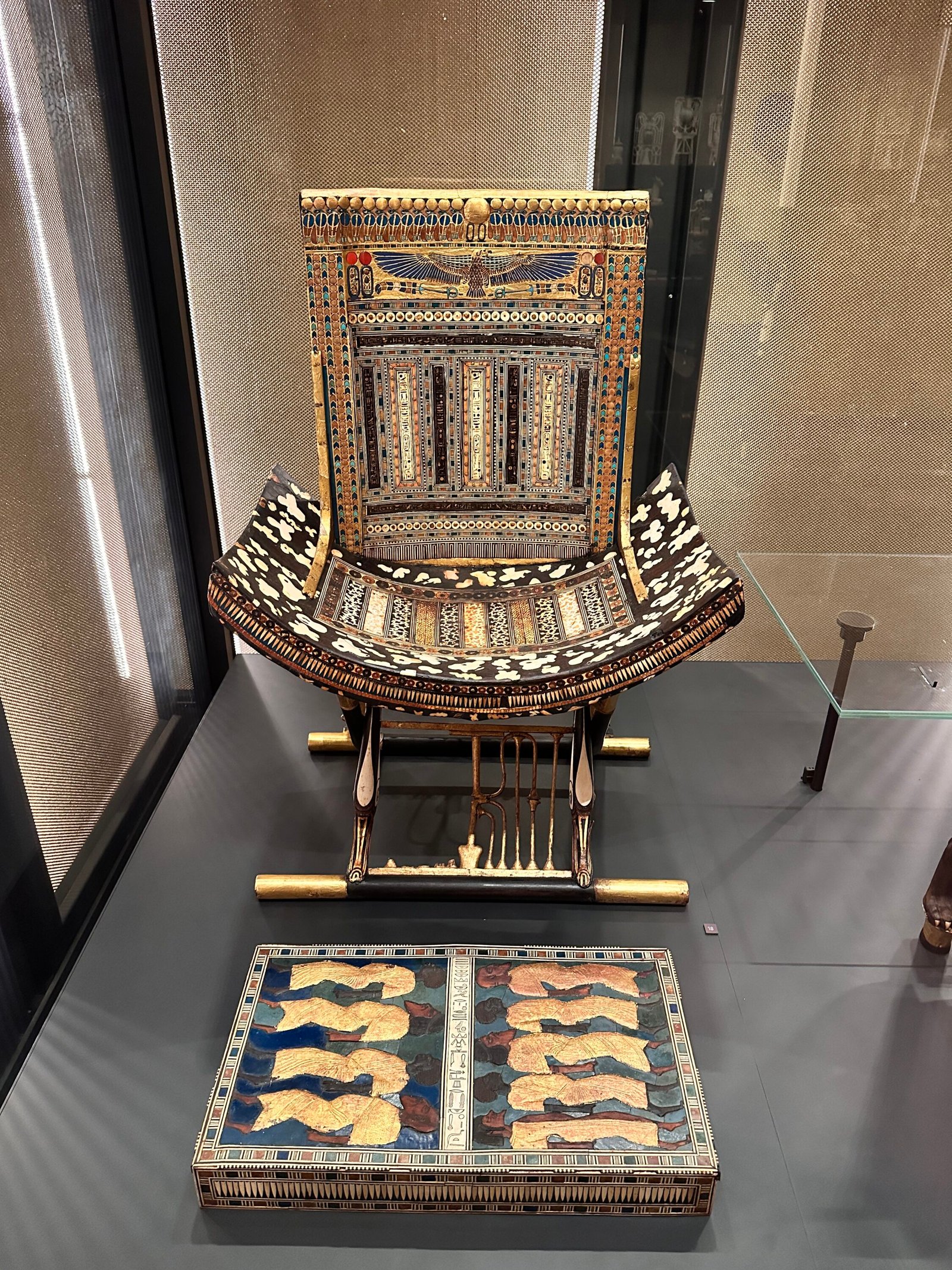 Ceremonial folding chair of Tutankhamun, JE 62030 / Carter 351, with spotted animal-skin seat, duck-head legs, sema-tawy brace and winged Nekhbet on the back, with JE 62045 footstool in front