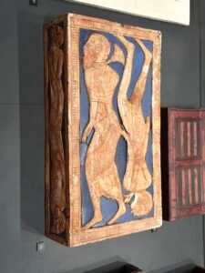 Ancient Egyptian painted furniture panel showing bound or inverted captive figures against a blue background at the Grand Egyptian Museum
