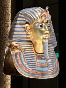 Golden burial mask of Pharaoh Tutankhamun, GEM 8, with blue-glass nemes stripes, uraeus and vulture emblems, broad collar and ceremonial beard at the Grand Egyptian Museum in Giza