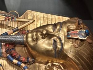 Close-up of the gilded face, nemes headdress, uraeus and vulture emblems on Tutankhamun's outer coffin, GEM 7590, at the Grand Egyptian Museum in Giza
