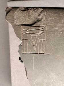 Close-up of a broken dark stone artifact with a small panel of carved Egyptian hieroglyphs