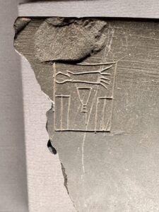 Broken dark stone fragment in the Egyptian Museum in Cairo preserving part of a royal serekh with the niched palace-facade design and carved hieroglyphic signs