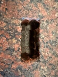 Close-up of a narrow rectangular mortise cut into polished red-and-black granite stone