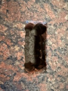 Close-up of a narrow rectangular mortise cut into polished red-and-black granite stone