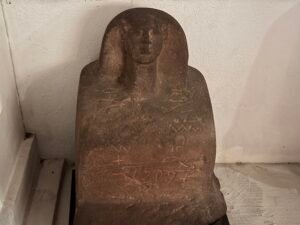 Dark stone funerary stela with a faint carved human figure above worn inscriptions