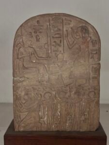 Ancient Egyptian stela with a seated figure, standing worshipper, and carved hieroglyphic inscriptions