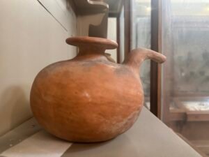 Predynastic Egyptian red-polished pottery jar with a globular body, wide flared rim and curved shoulder spout, displayed at the Egyptian Museum in Cairo