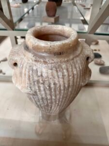 Pale hard-stone jar with deep vertical fluting, broad rim and two pierced lug handles, a Predynastic to Early Dynastic vessel type at the Egyptian Museum in Cairo