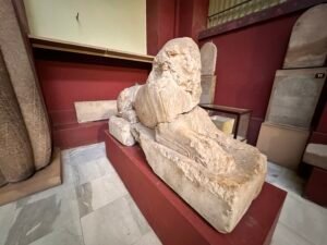 Weathered ancient Egyptian sphinx statue with human head and lion body displayed on a museum platform