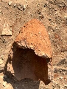 Large reddish-brown ancient pottery fragment lying on sandy ground on the Giza Plateau