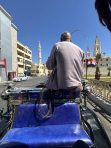 View from a blue horse-drawn carriage traveling along a Cairo street with churches, minarets, and Egyptian flags