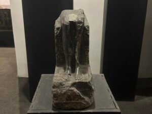 Fragmentary dark stone Egyptian statue preserving the lower body, legs, feet, and hieroglyphic inscriptions