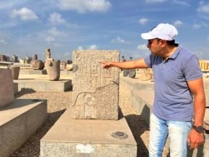 Guide pointing to hieroglyphs and a carved figure on an inscribed granite monument in the open-air museum at Tell Basta, ancient Bubastis, in Zagazig