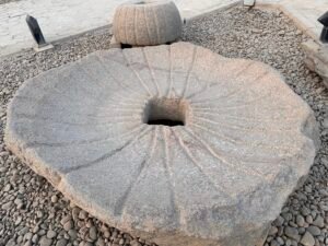 Large circular granite block with radiating carved channels and a square central socket in the Matariya Open-Air Museum at ancient Heliopolis, Cairo