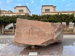 Large reddish granite block with an oversized royal cartouche and hieroglyphic signs displayed at the Matariya Open-Air Museum at ancient Heliopolis in Cairo