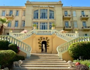 Historic Winter Palace hotel facade in Luxor with a sweeping double staircase, gardens, and tall windows
